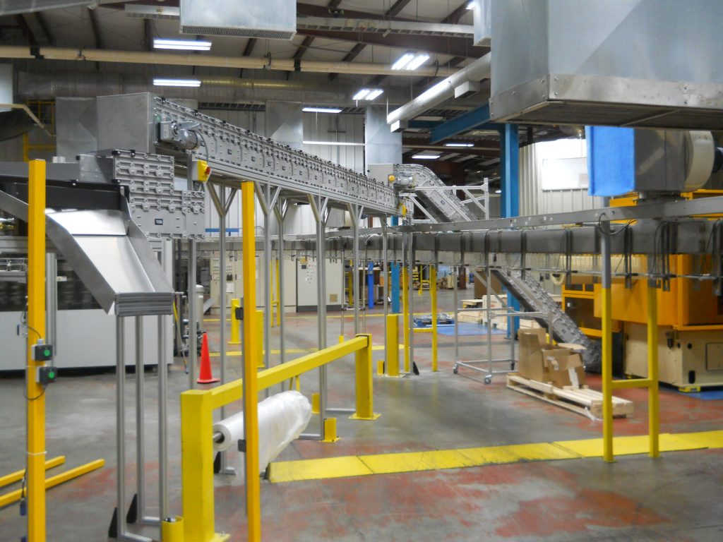 A DynaCon incline conveyor feeding plastic parts from a machine up to a flat overhead conveyor.