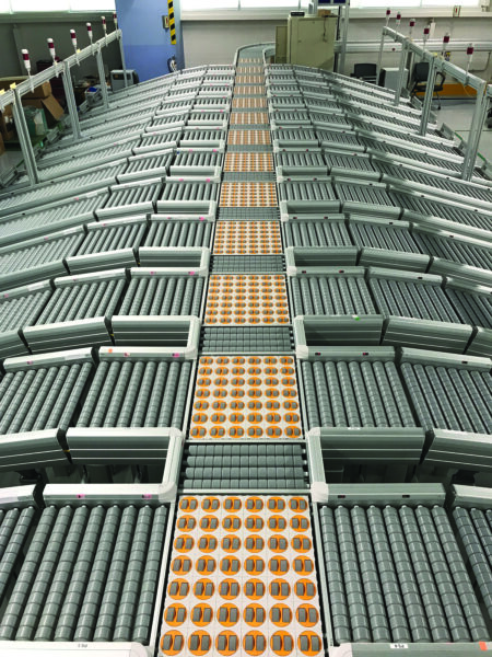 A close-up view of many roller conveyors that feed into a long zone powered transfer conveyor in a distribution center