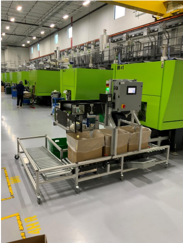 A box filling conveyor with a right angle roller conveyor attached in a factory with bright green machinery