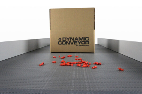A close-up of the belting on a DynaPro conveyor with small red plastic pieces and a box on top of the belt