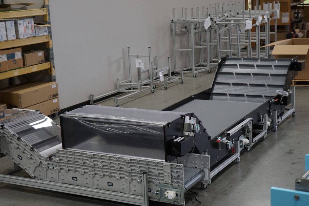 Hybrid Wide Multiple Interlocking Conveyors An extra wide conveyor with multiple interlocking conveyors for a custom conveyor application in a factory with boxes and portable casters in the background