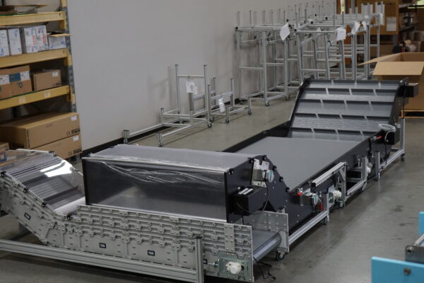 An extra wide conveyor with multiple interlocking conveyors for a custom conveyor application in a factory with boxes and portable casters in the background