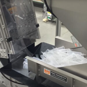 A close up of plastic syringes entering the bottom of a DynaCon bucket conveyor