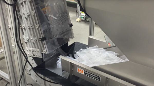 A close up of plastic syringes entering the bottom of a DynaCon bucket conveyor