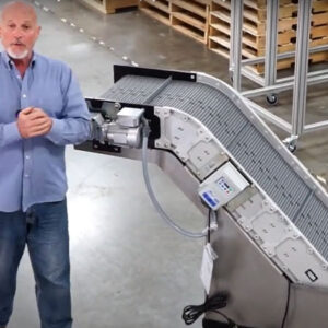 An older man standing next to a Hybrid incline conveyor with a water bath tank