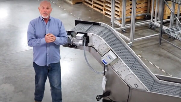 An older man standing next to a Hybrid incline conveyor with a water bath tank