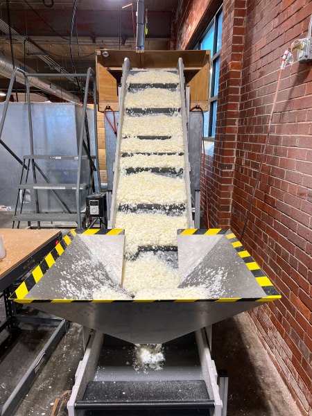Candle wax being transported down an incline conveyor into a hopper