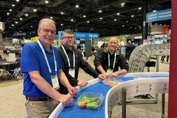 dynamic-conveyor-eats-2025 Dynamic Conveyor staff standing around curved sanitary conveyor at EATS show