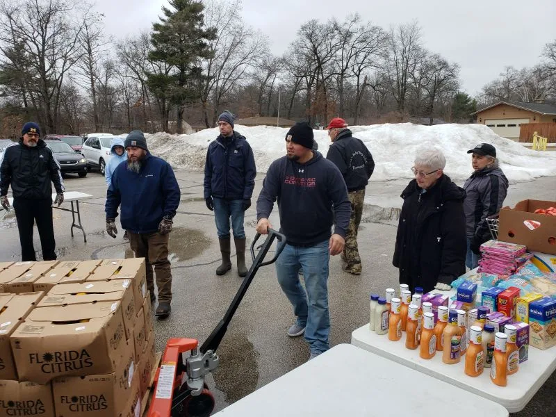feeding-america-volunteers-2026-6 table full of donated food and workers moving pallet of Florida oranges