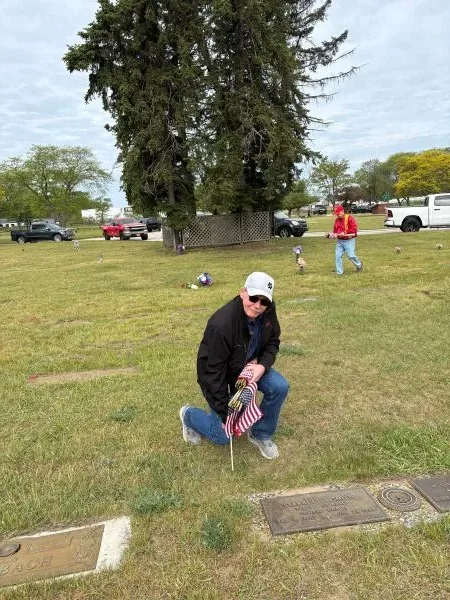 flag-veteran-memorial-2026 man placing flag on gravesite for veteran at Sunrise Memorial Gardens in Muskegon