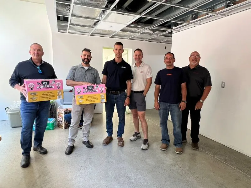 Jeff-Team-lesser-evil-snacks Dynamic Conveyor and Troy Industrial Solutions staff standing with Lesser Evil snack boxes at manufacturing facility